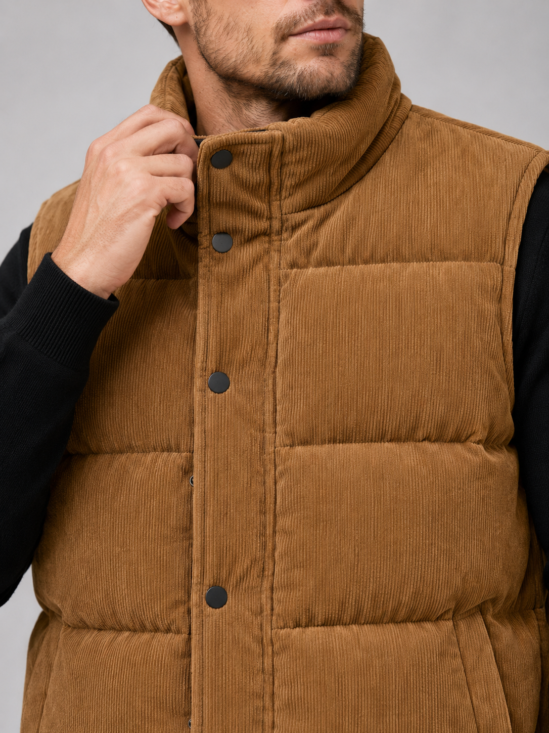 Close-up of a brown corduroy puffer vest showing the ribbed fabric texture, thick padding, stand collar, zipper, pockets, armholes, and stitching