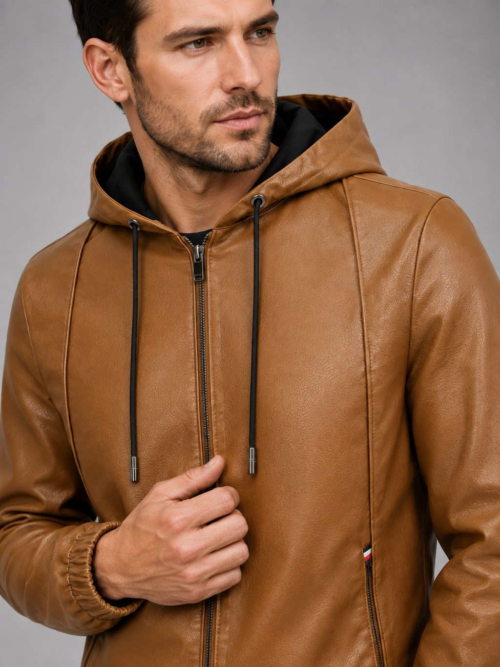 Close-up of a brown hooded leather jacket showing the premium leather texture, zip-up closure, hood, stitching, cuffs, pockets, and warm interior finish