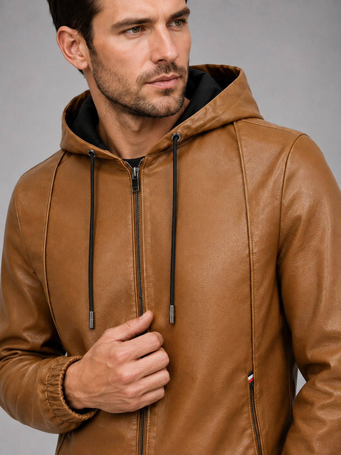 Close-up of a brown hooded leather jacket showing the premium leather texture, zip-up closure, hood, stitching, cuffs, pockets, and warm interior finish