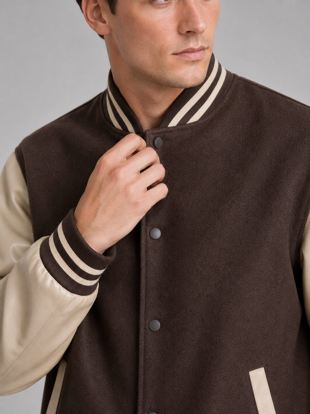 Close up of brown varsity jacket showing smooth leather sleeves, wool blend fabric, and snap button detail