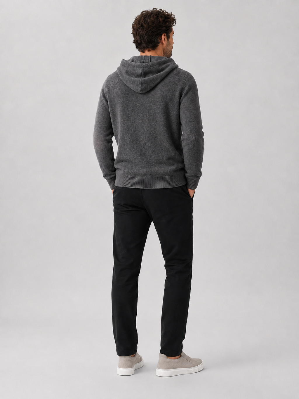 Back view of a man wearing a dark gray wool hoodie sweater showing the attached hood, long sleeves, and relaxed fit