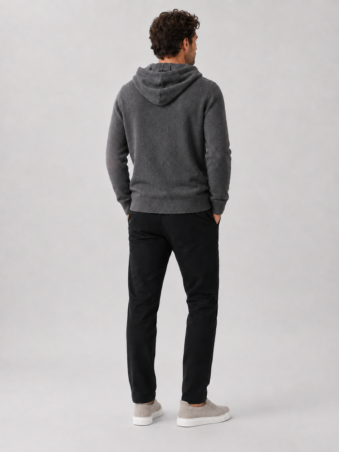 Back view of a man wearing a dark gray wool hoodie sweater showing the attached hood, long sleeves, and relaxed fit