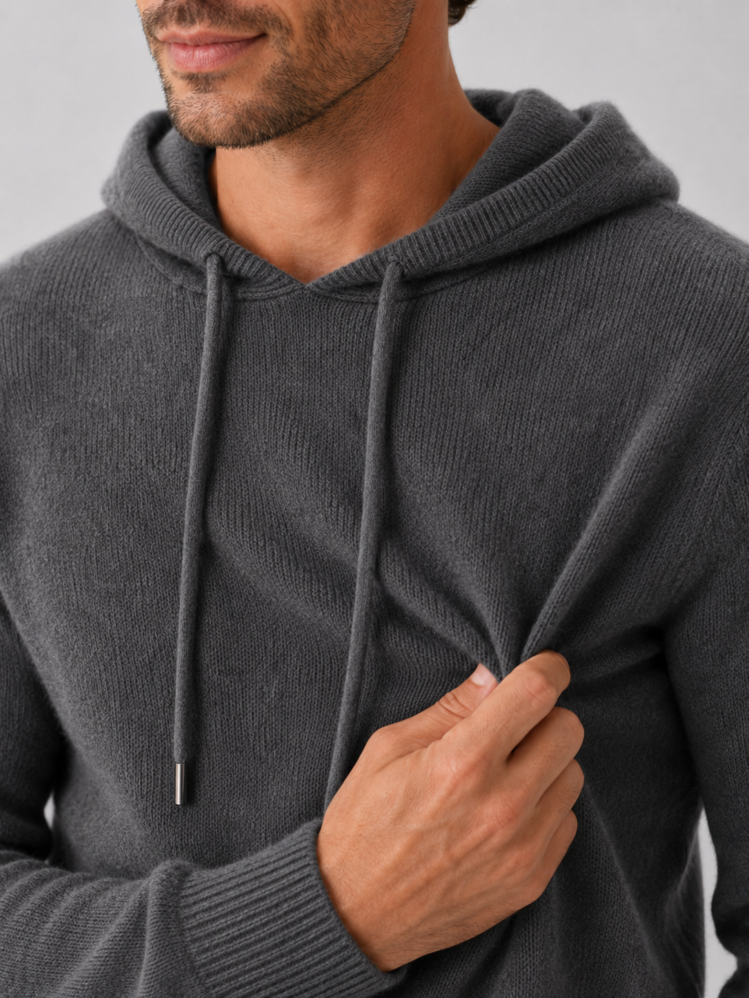 Close-up of a dark gray wool hoodie sweater showing the soft knit texture, hood, ribbed cuffs, hem, and stitching details