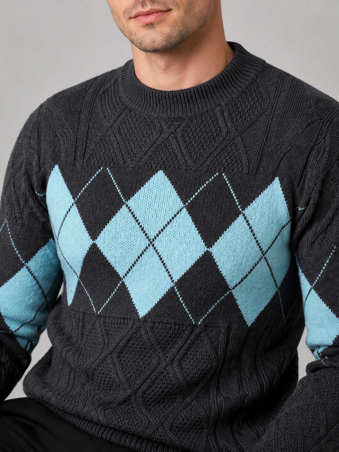 Close-up of a gray argyle cable knit sweater showing the cable knit texture, argyle pattern, patchwork details, mock neck, ribbed cuffs, and hem