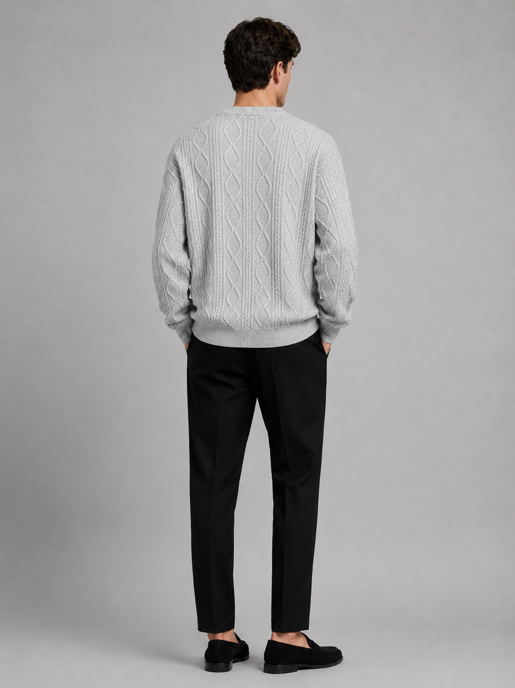 Back view of a man wearing a gray cable knit cardigan sweater showing the relaxed oversized fit, long sleeves, and warm knit construction