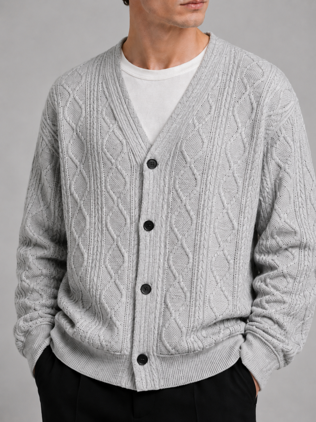 Close-up of a gray cable knit cardigan showing the diamond pattern, textured cable knit, V-neckline, front buttons, ribbed cuffs, and hem