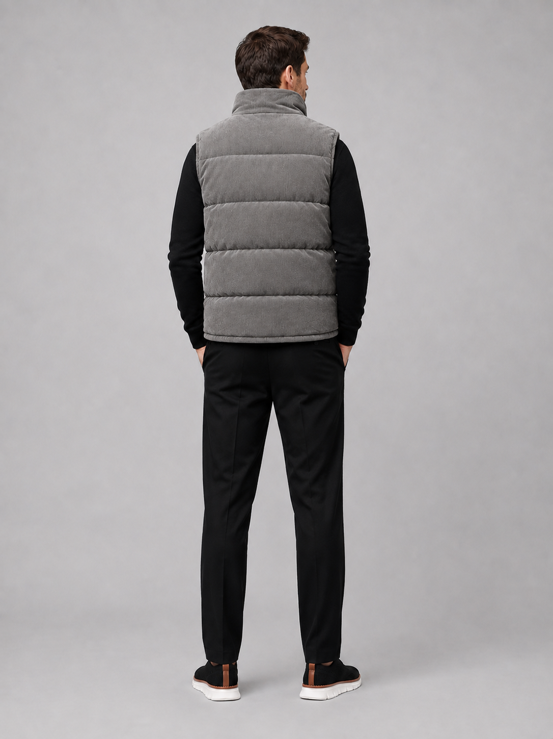 Back view of a man wearing a gray corduroy puffer vest showing the sleeveless cut, padded construction, and comfortable fit