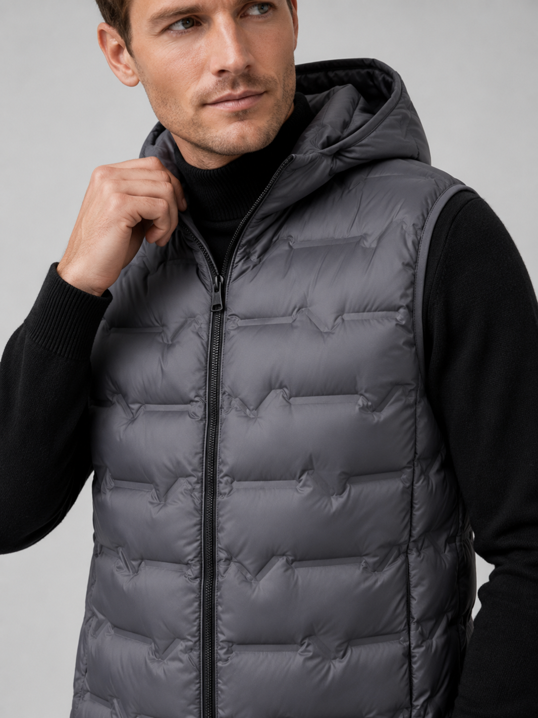 Close up of gray hooded down vest showing lightweight quilted insulation, attached hood, and weather resistant fabric detail