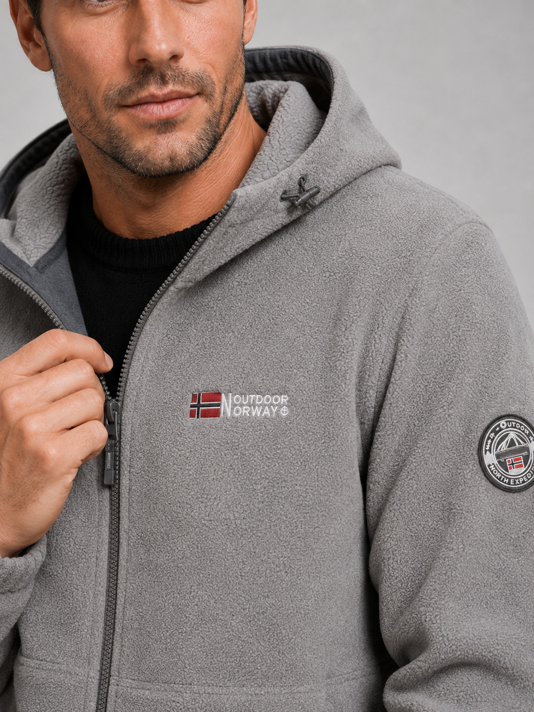Close-up of a gray hooded fleece jacket showing the soft fleece texture, windproof construction, full zipper, hood, pockets, cuffs, and stitching details