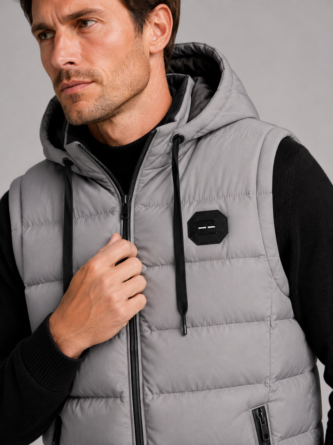 Close-up of a gray hooded puffer vest showing the cotton padding, thick insulation, zipper closure, hood, pockets, armholes, and stitching details