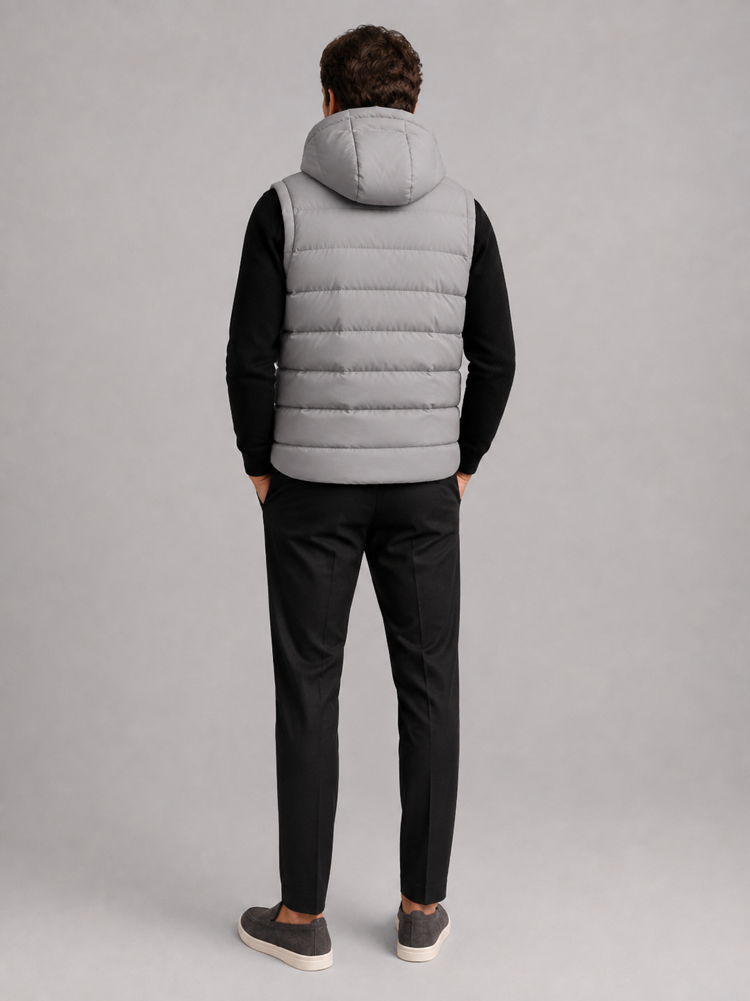 Back view of a man wearing a gray hooded puffer vest showing the attached hood, padded construction, sleeveless cut, and comfortable fit