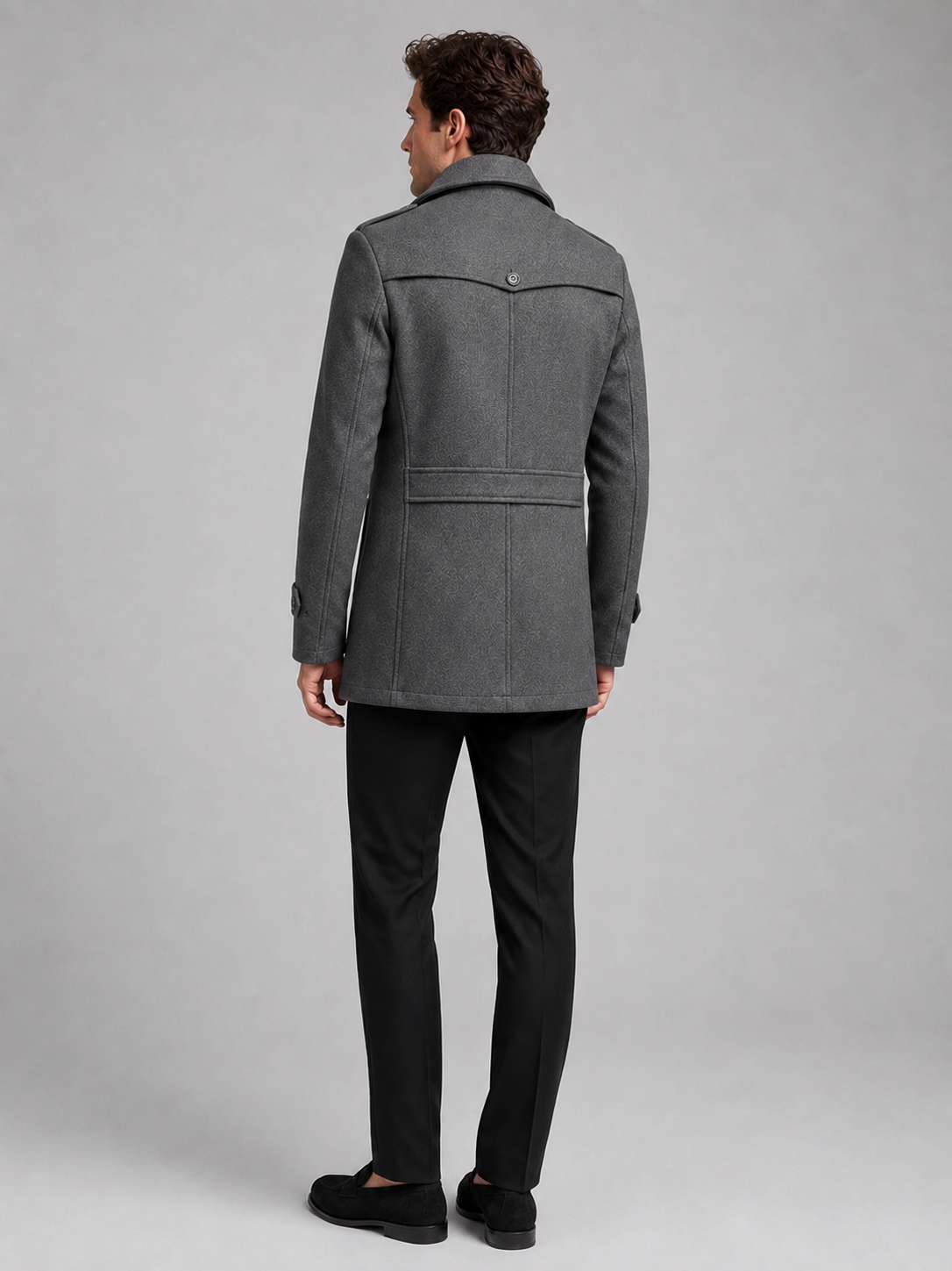 Back view of a man wearing a gray wool coat showing the structured shoulders, long silhouette, and tailored fit
