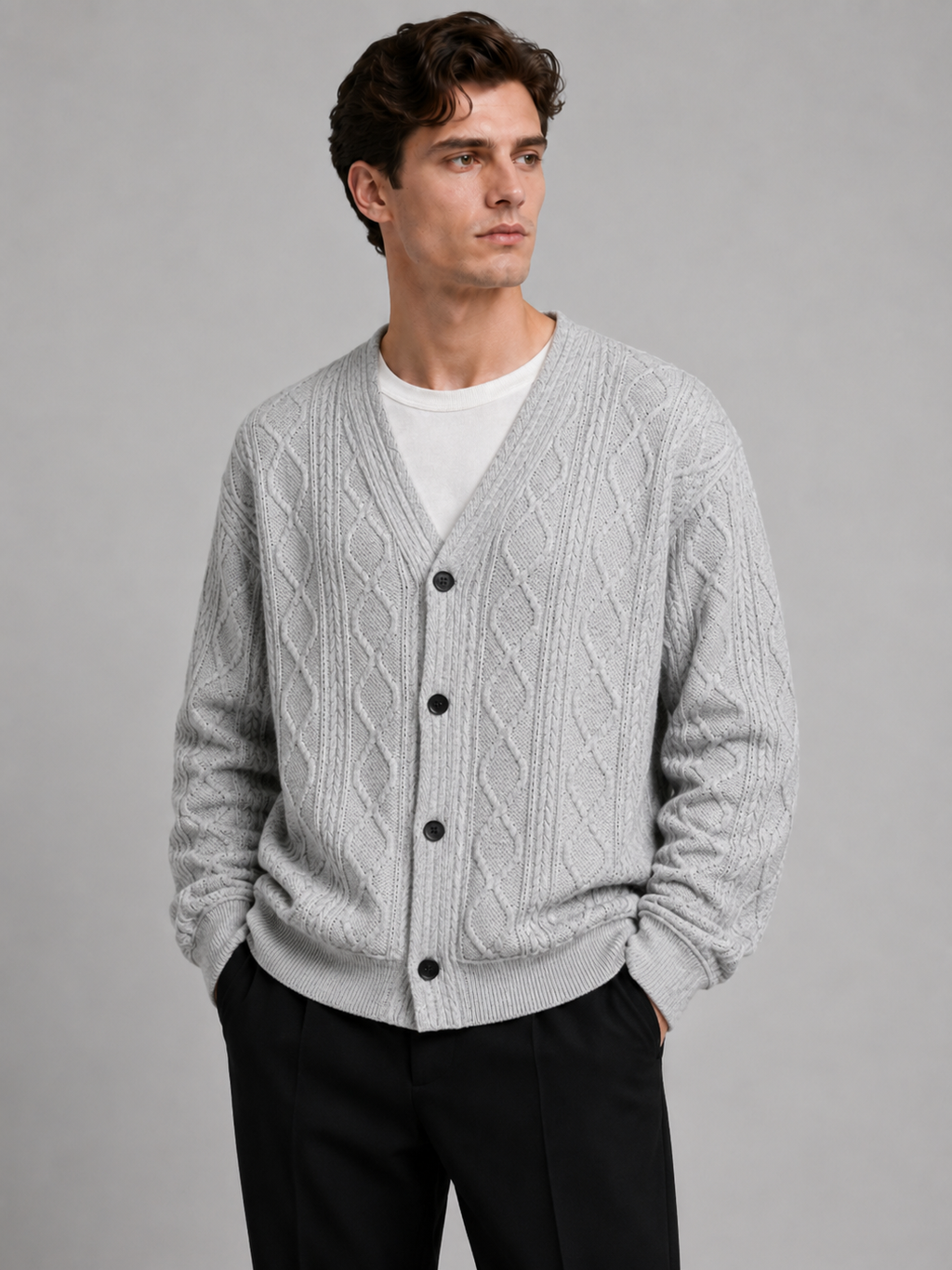 Front view of a man wearing a gray cable knit cardigan sweater with a V-neck, diamond pattern, button-front design, and oversized fit