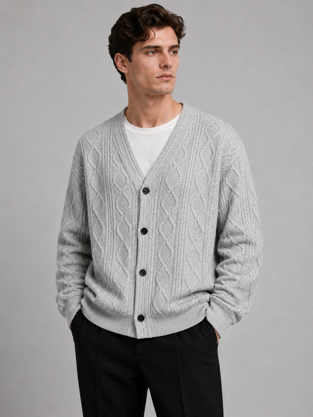 Front view of a man wearing a gray cable knit cardigan sweater with a V-neck, diamond pattern, button-front design, and oversized fit
