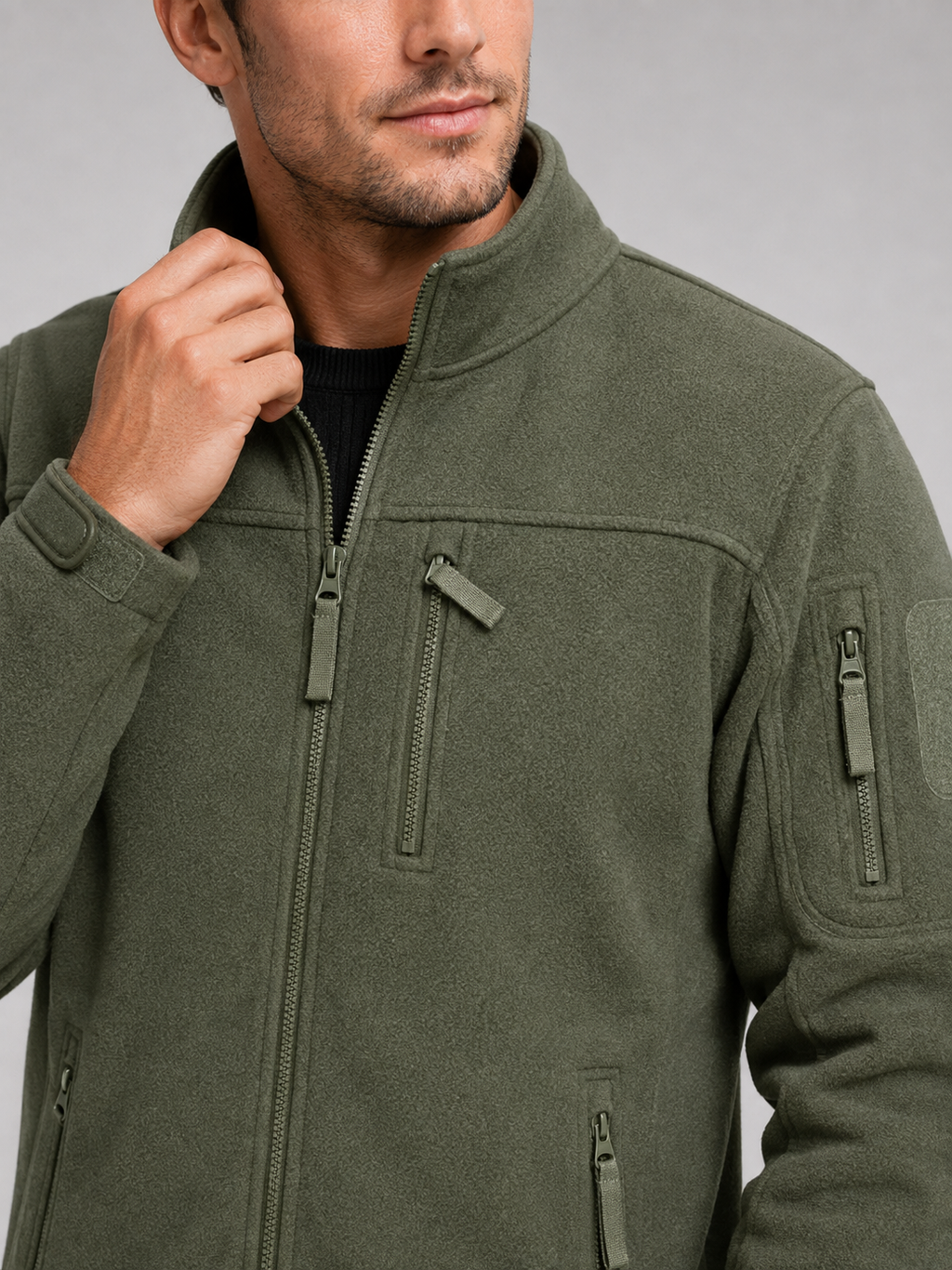 Close-up of a green windproof fleece jacket showing the soft fleece texture, full zipper, zippered pockets, collar, cuffs, hem, and stitching details