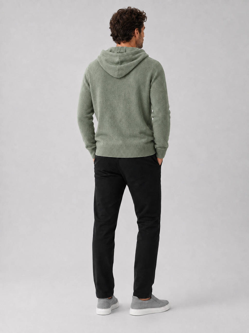 Back view of a man wearing a green wool hoodie sweater showing the attached hood, long sleeves, and relaxed fit