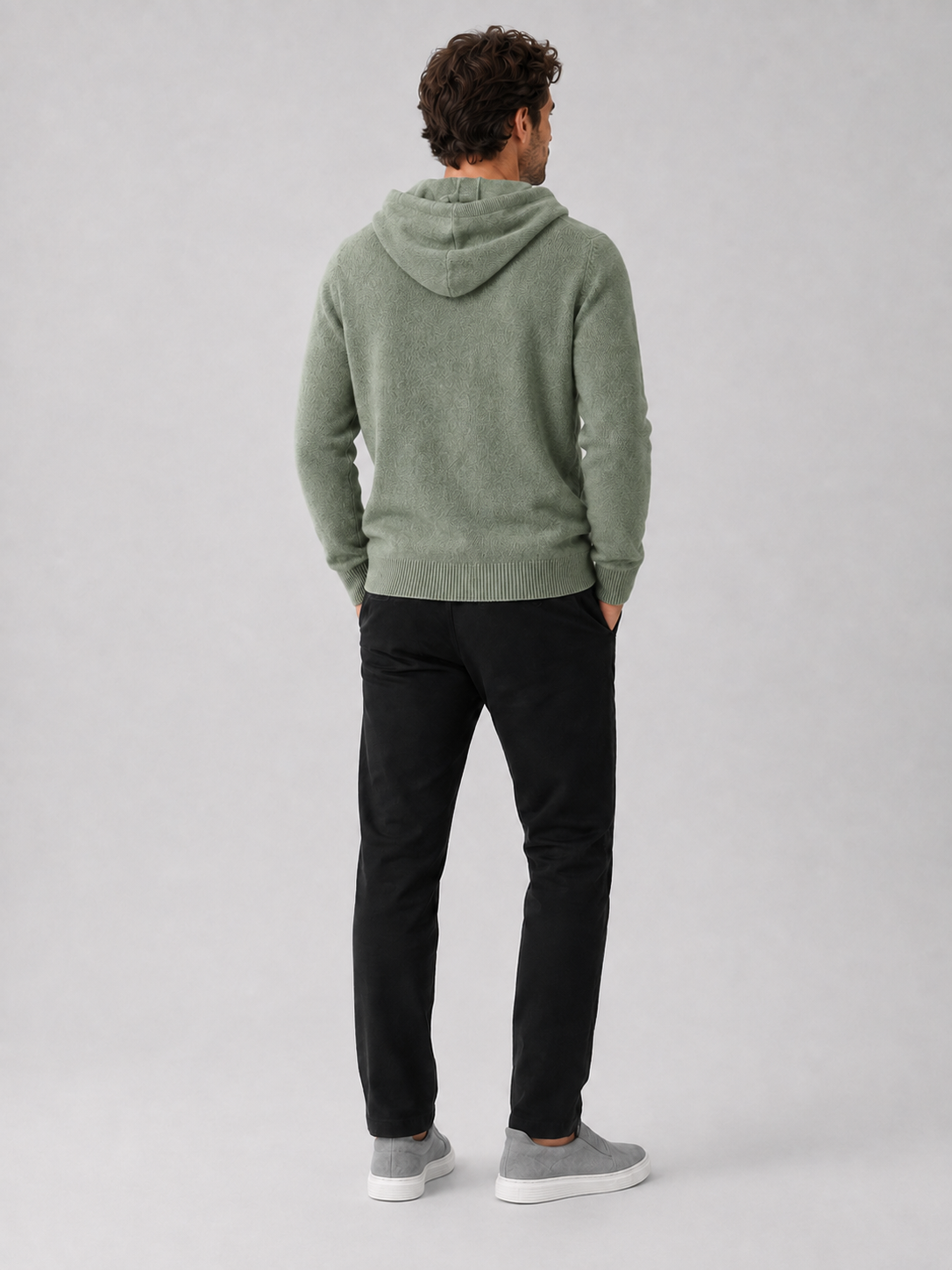Back view of a man wearing a green wool hoodie sweater showing the attached hood, long sleeves, and relaxed fit