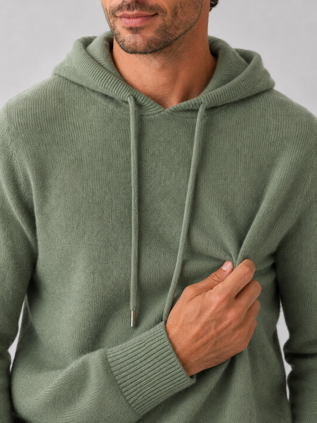 Close-up of a green wool hoodie sweater showing the soft knit texture, hood, ribbed cuffs, hem, and stitching details