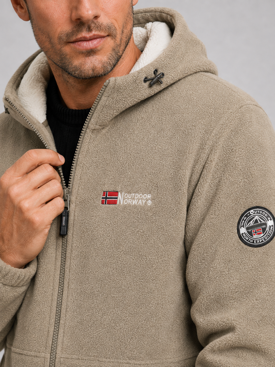 Close-up of a khaki hooded fleece jacket showing the soft fleece texture, windproof construction, full zipper, hood, pockets, cuffs, and stitching details