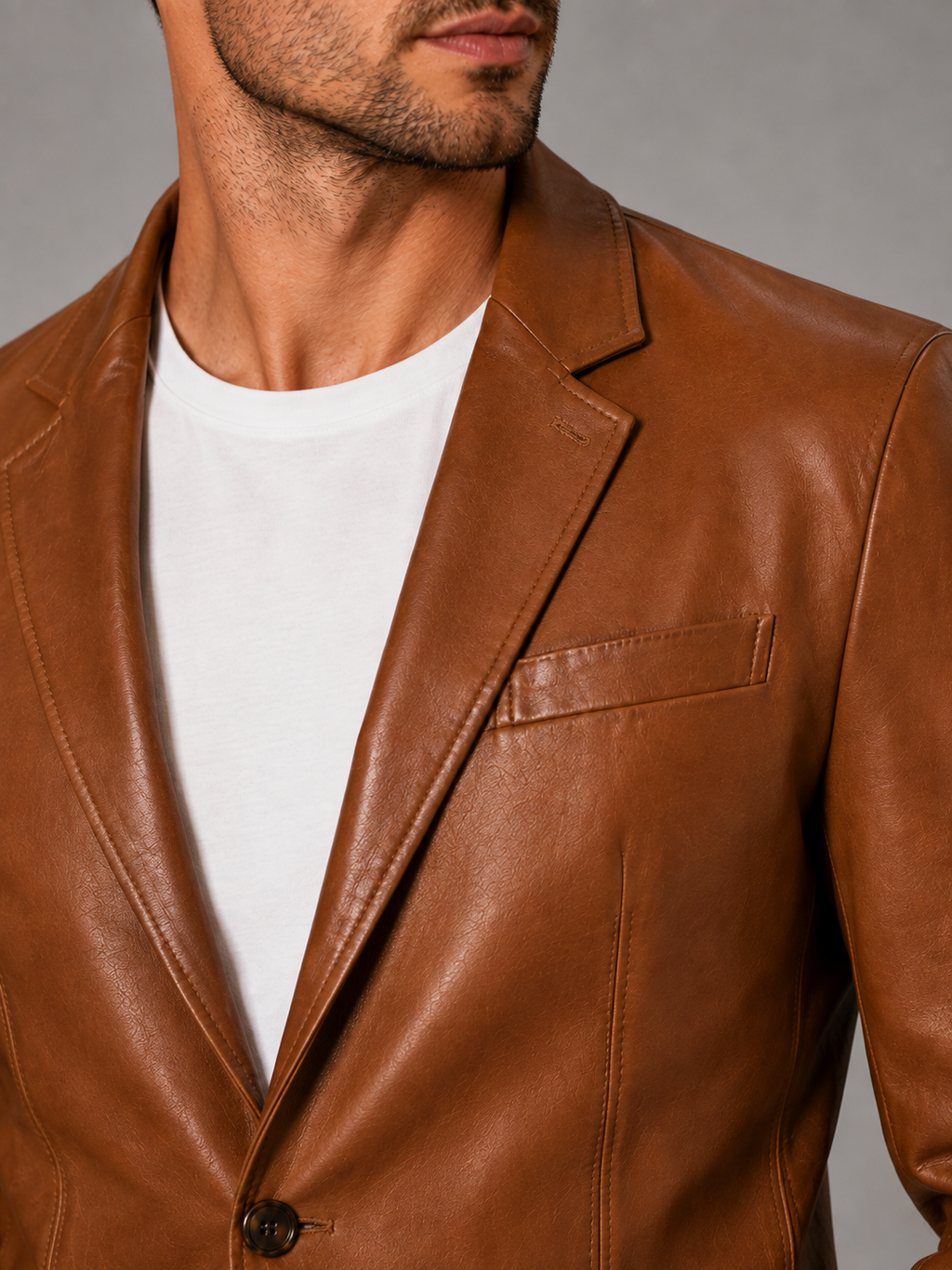 Close-up of a khaki leather blazer jacket showing the premium leather texture, notched lapel, button closure, tailored stitching, cuffs, and pocket details