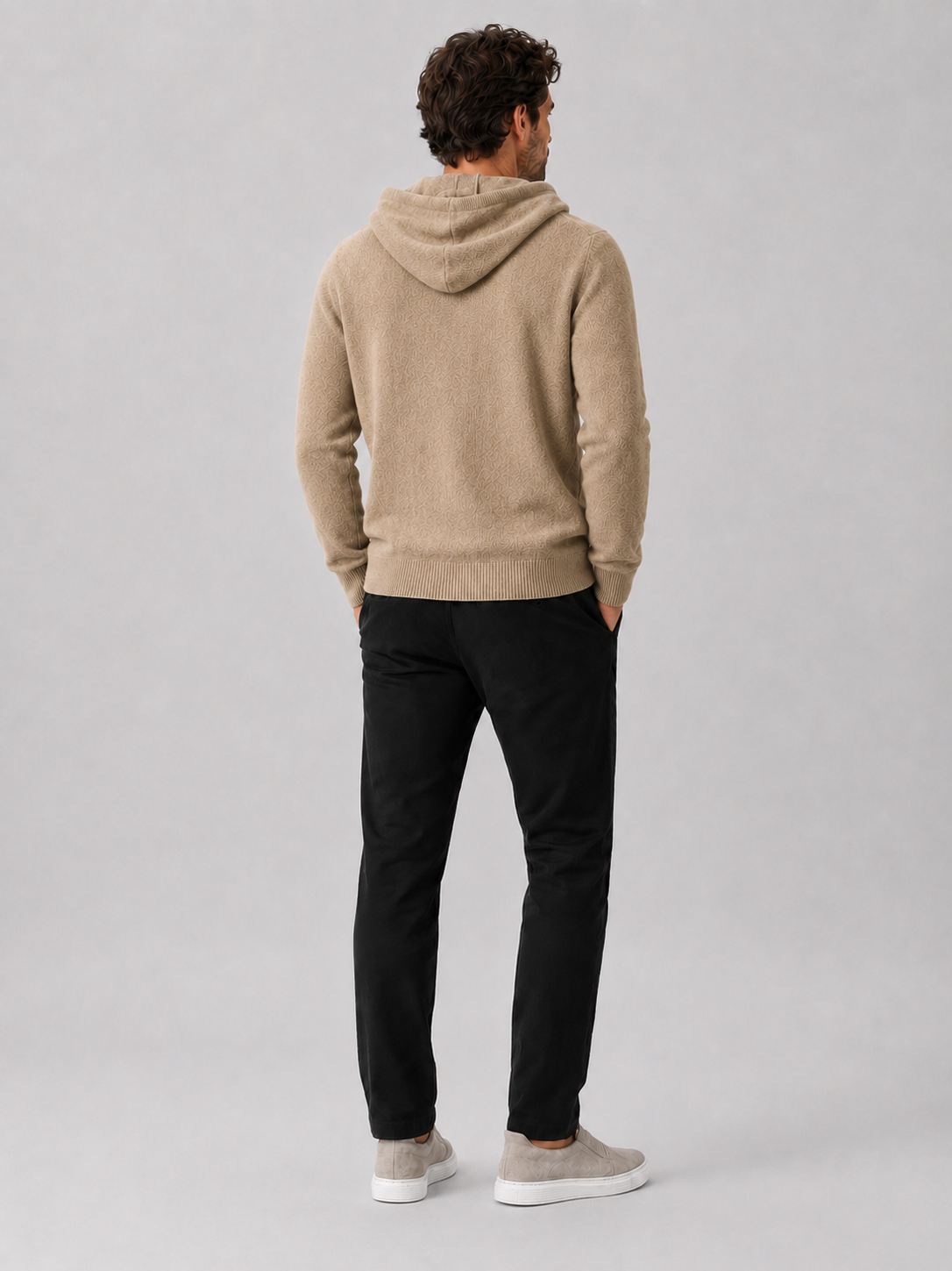 Back view of a man wearing a khaki wool hoodie sweater showing the attached hood, long sleeves, and relaxed fit