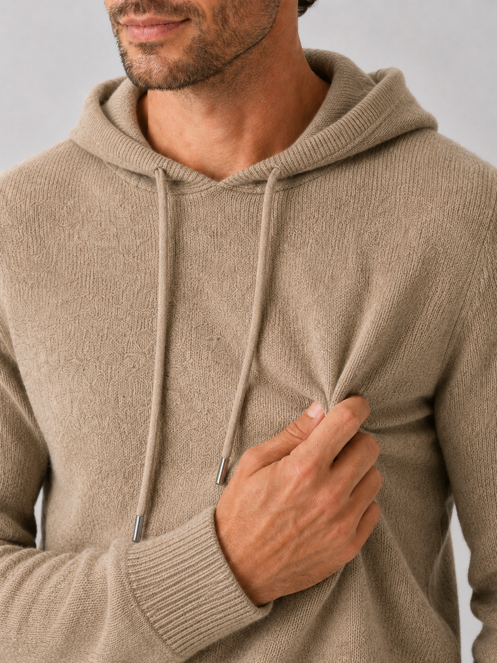 Close-up of a khaki wool hoodie sweater showing the soft knit texture, hood, ribbed cuffs, hem, and stitching details