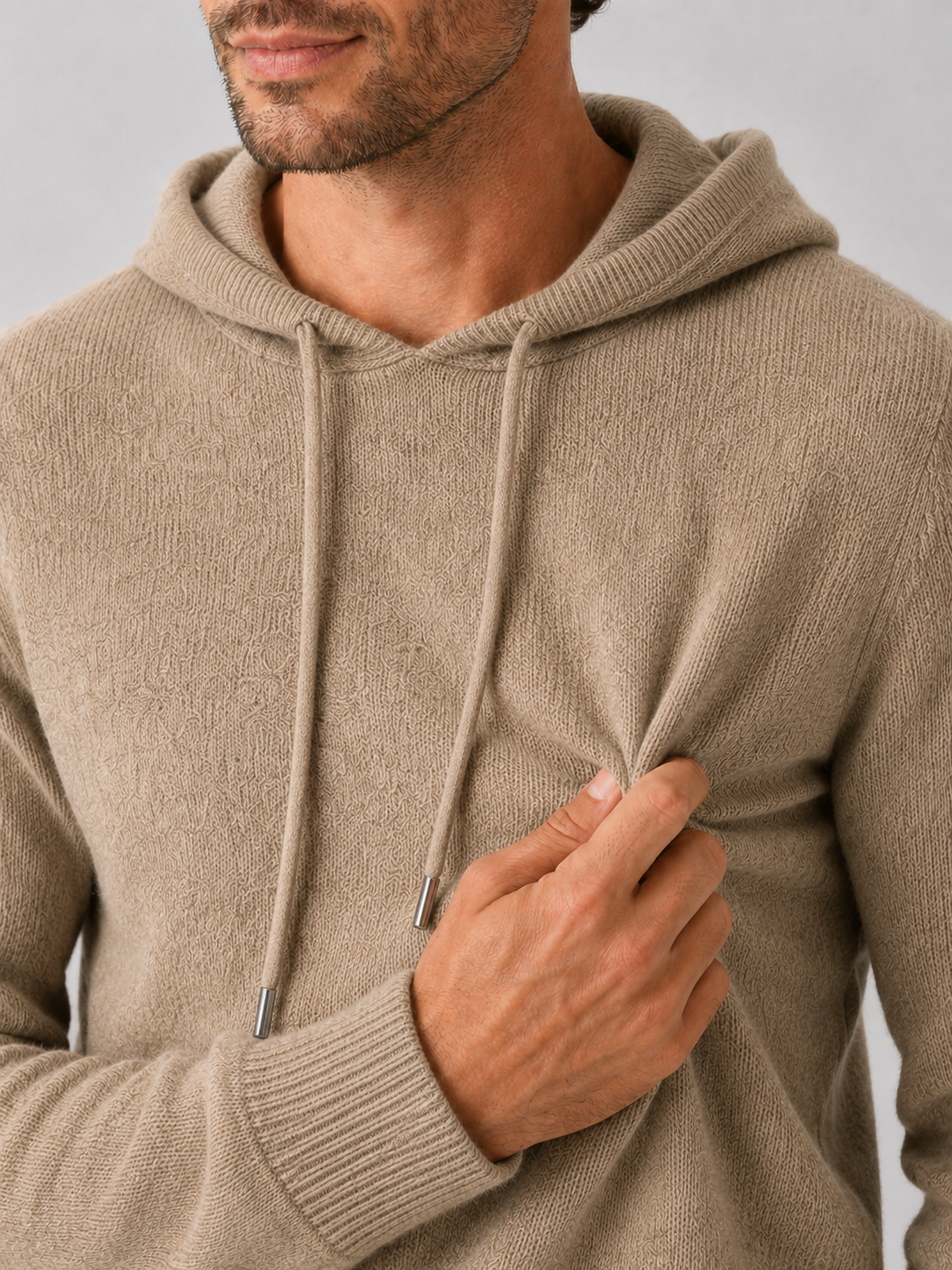 Close-up of a khaki wool hoodie sweater showing the soft knit texture, hood, ribbed cuffs, hem, and stitching details