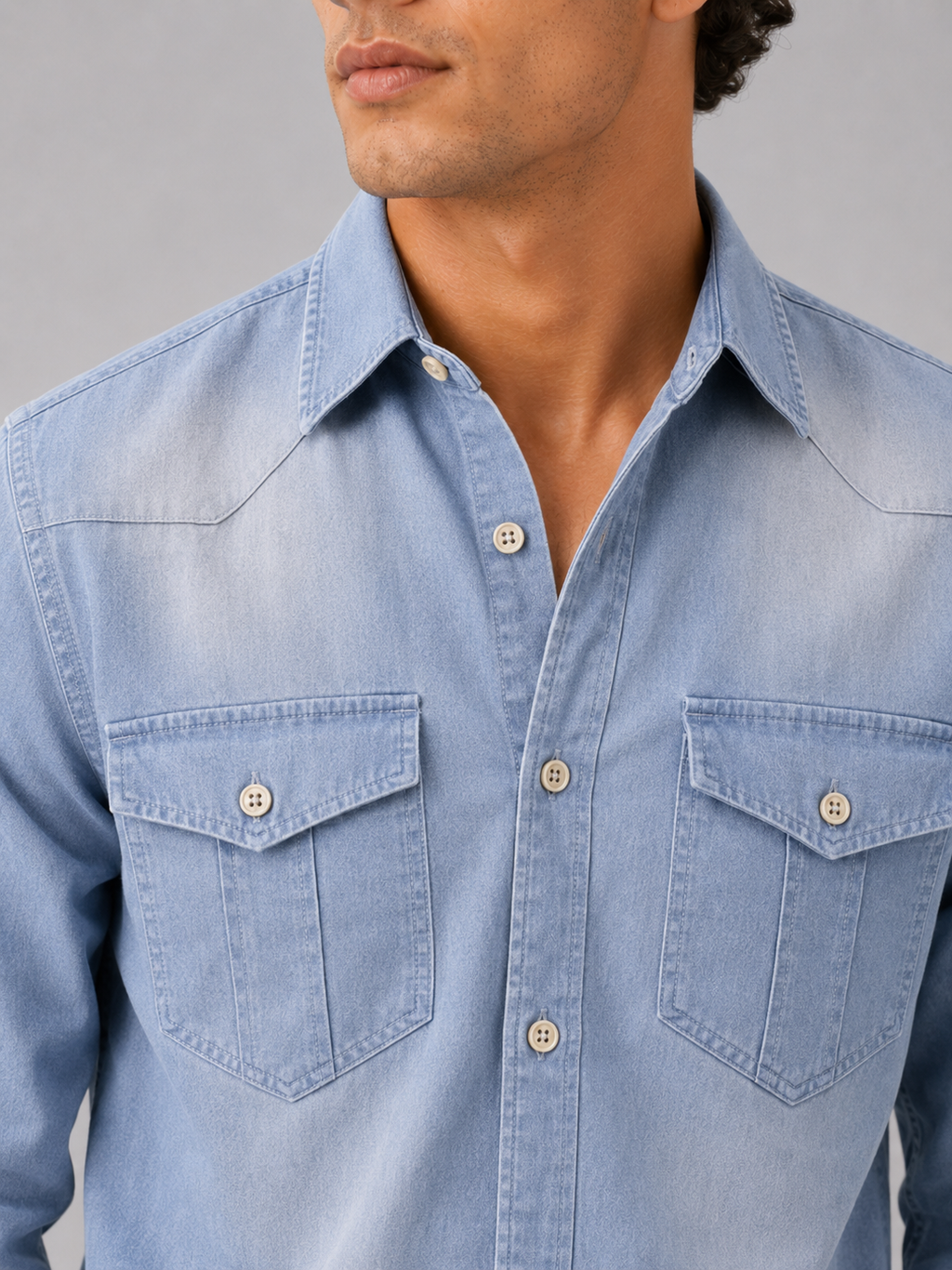 Close up of light blue denim shirt showing washed cotton texture and button up detail