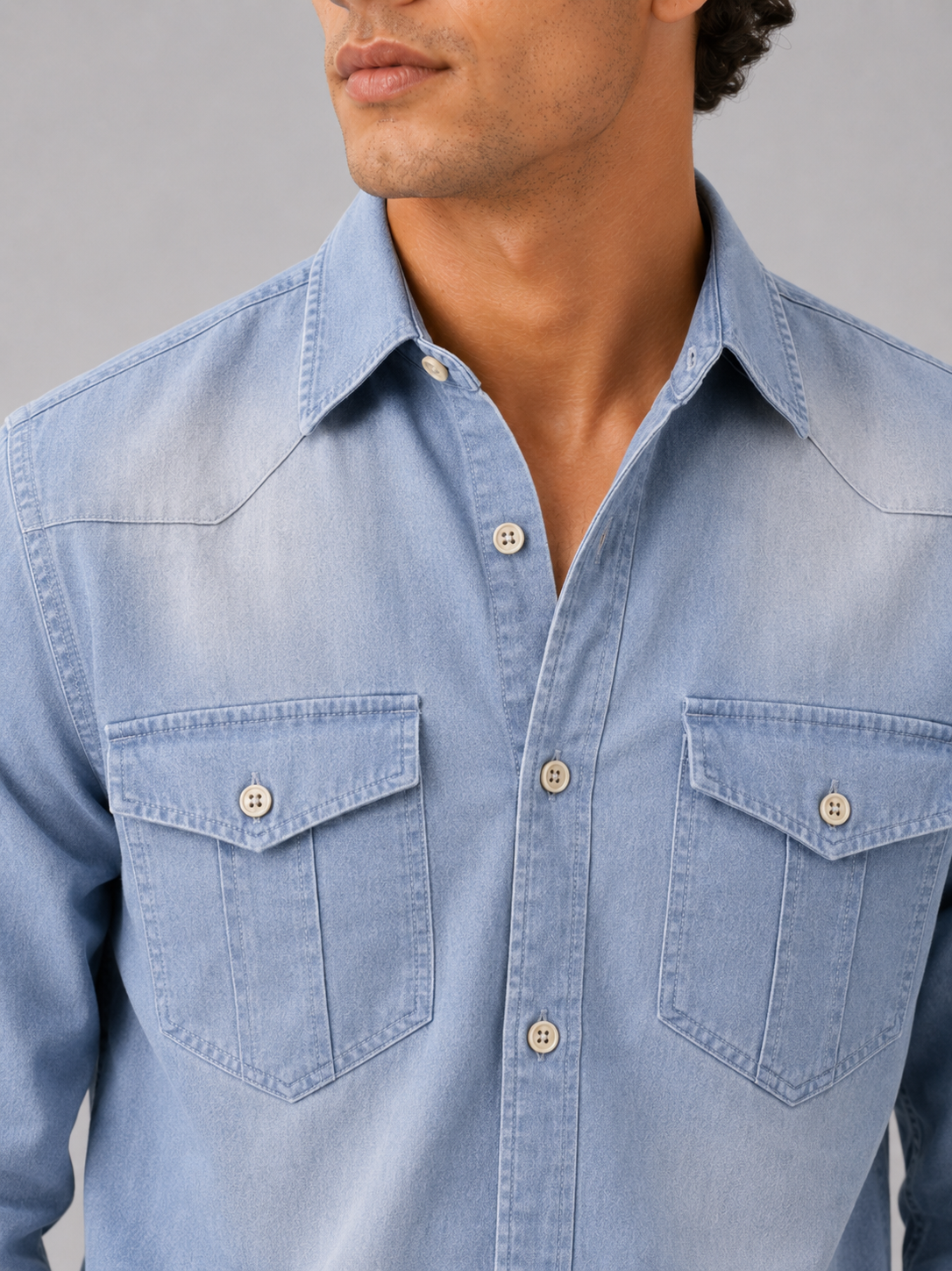 Close up of light blue denim shirt showing washed cotton texture and button up detail