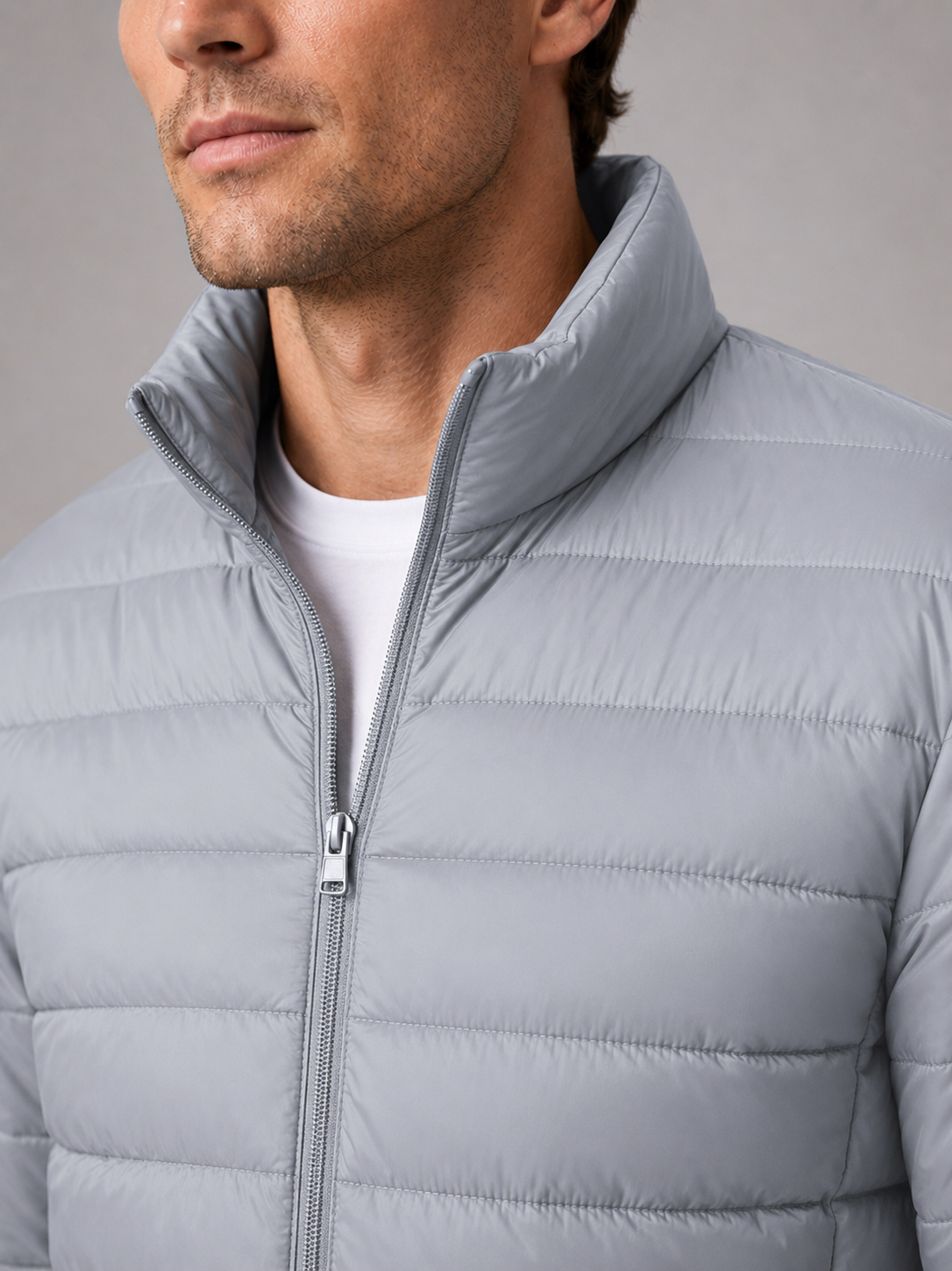 Close up of light gray down puffer jacket showing insulated quilting, stand collar, and weather resistant fabric detail