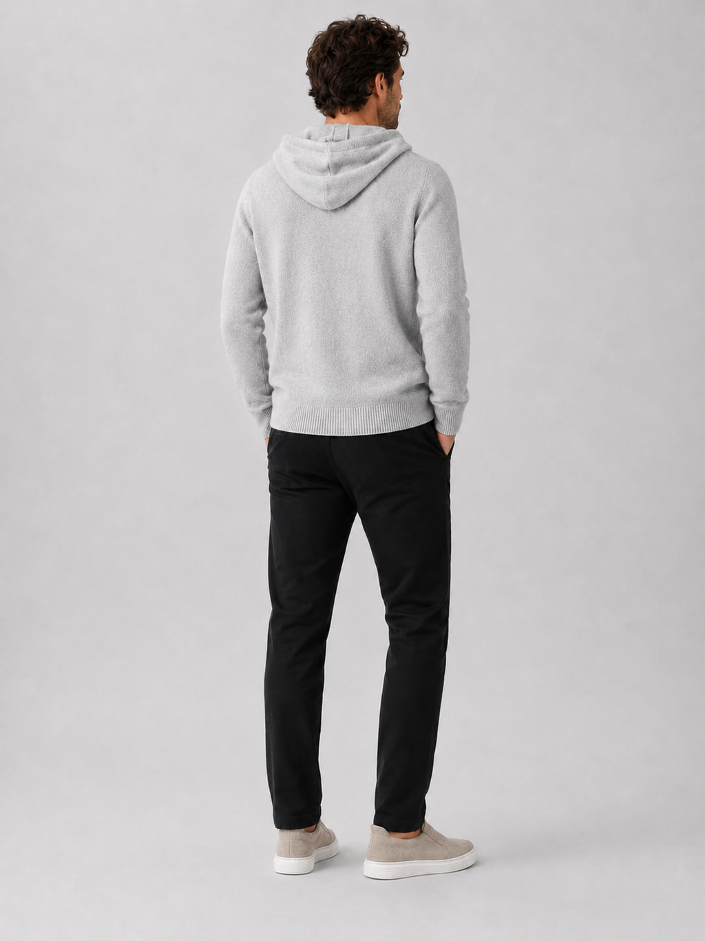 Back view of a man wearing a light gray wool hoodie sweater showing the attached hood, long sleeves, and relaxed fit