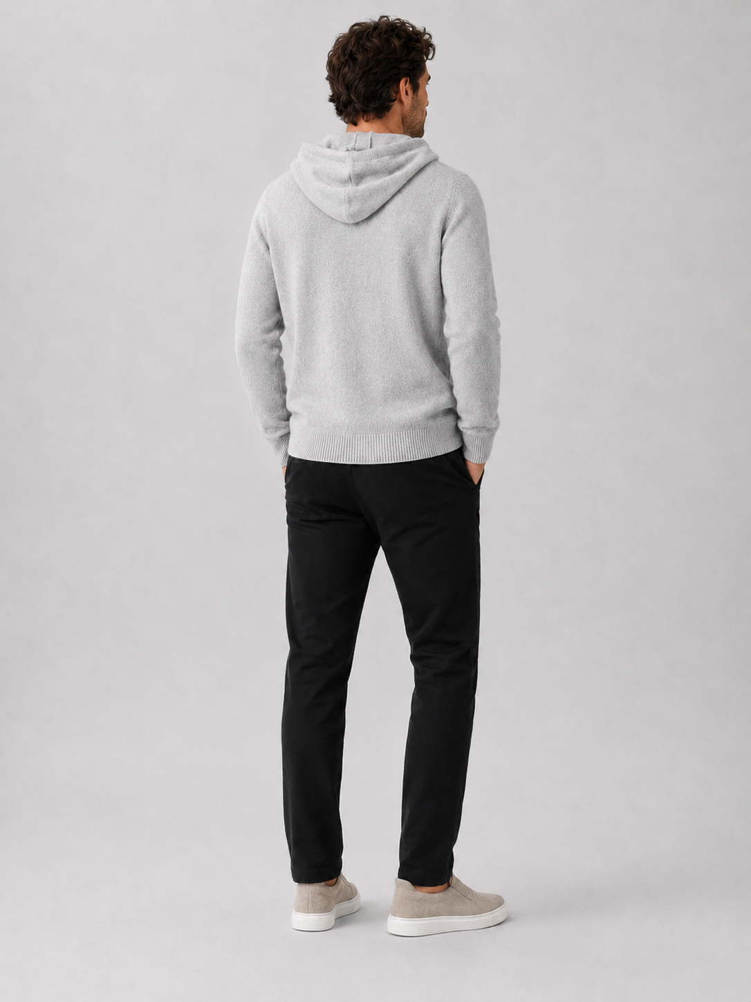 Back view of a man wearing a light gray wool hoodie sweater showing the attached hood, long sleeves, and relaxed fit