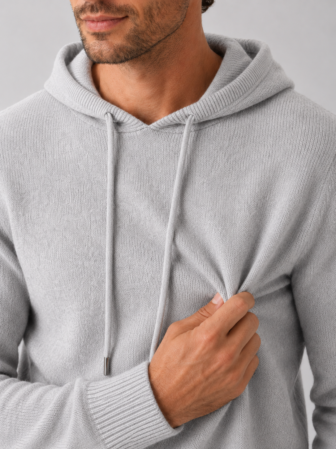 Close-up of a light gray wool hoodie sweater showing the soft knit texture, hood, ribbed cuffs, hem, and stitching details