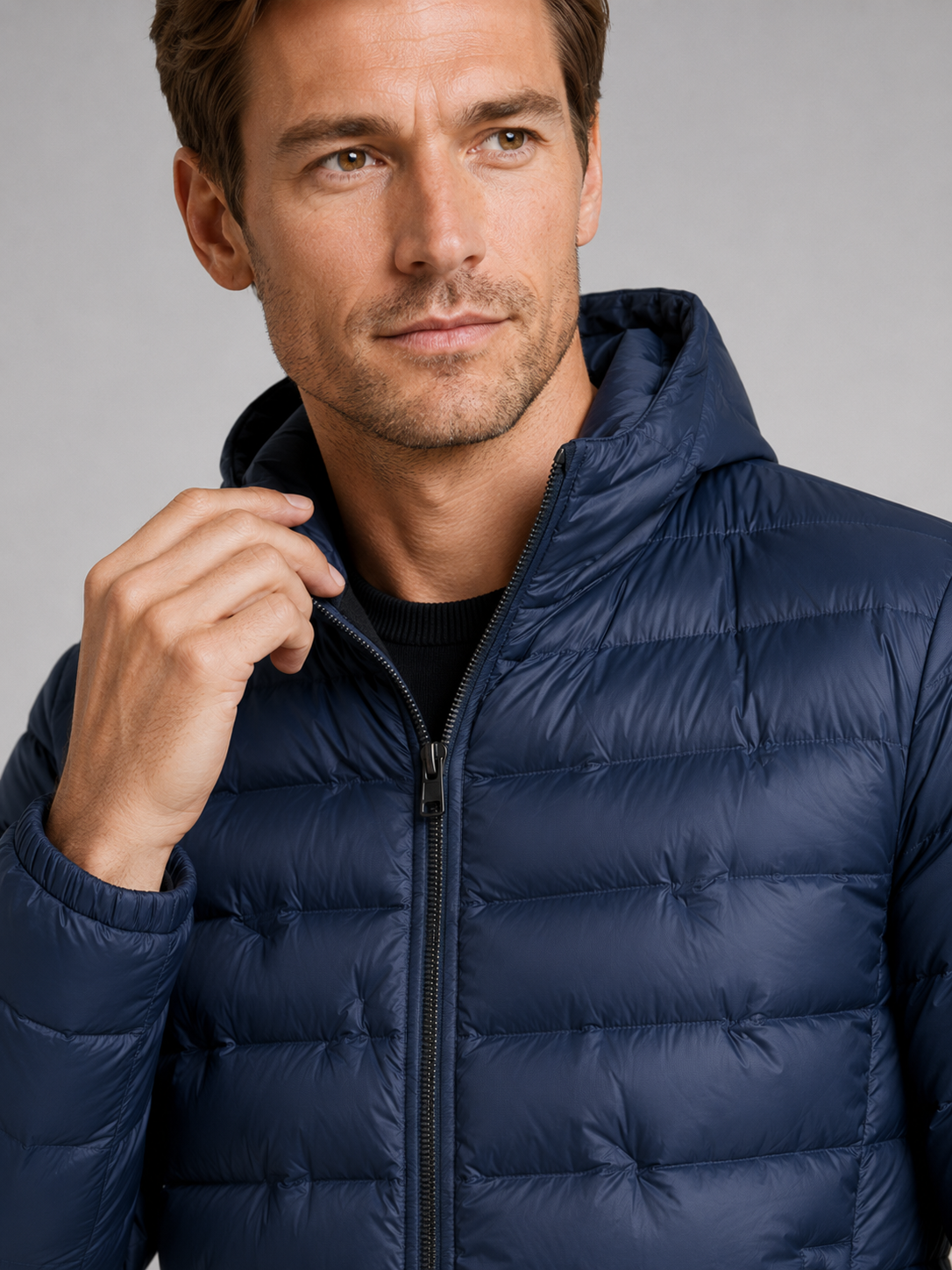 Close up of navy down puffer jacket showing lightweight quilted insulation, attached hood, and weather resistant fabric detail