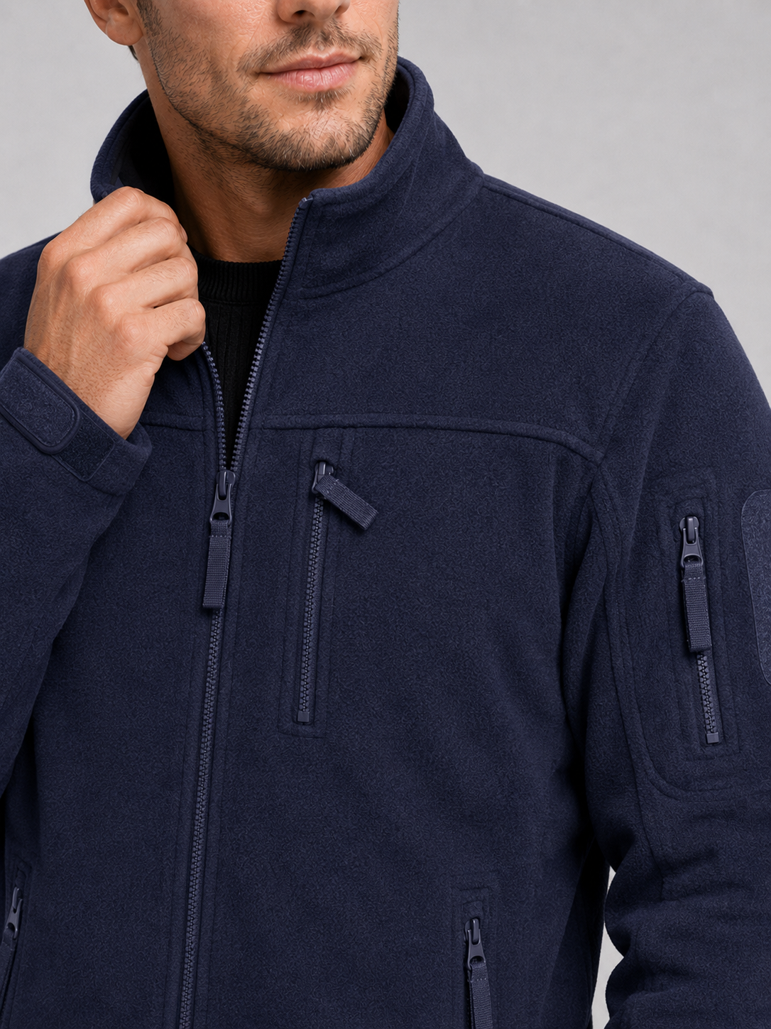 Close-up of a navy windproof fleece jacket showing the soft fleece texture, full zipper, zippered pockets, collar, cuffs, hem, and stitching details