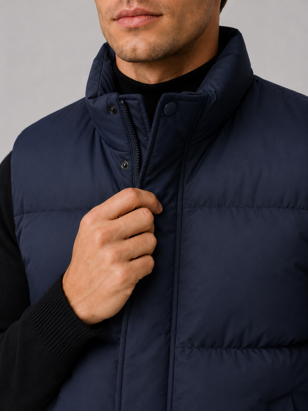 Close-up of a navy puffer vest showing the quilted insulation, full zipper, stand collar, pockets, stitching, and lightweight shell fabric