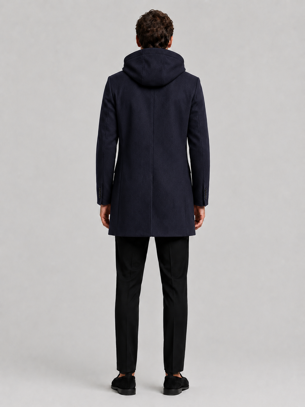 Backside photo of a man wearing a navy wool hooded trench coat, showing the hood, back seam, coat length, and tailored winter fit