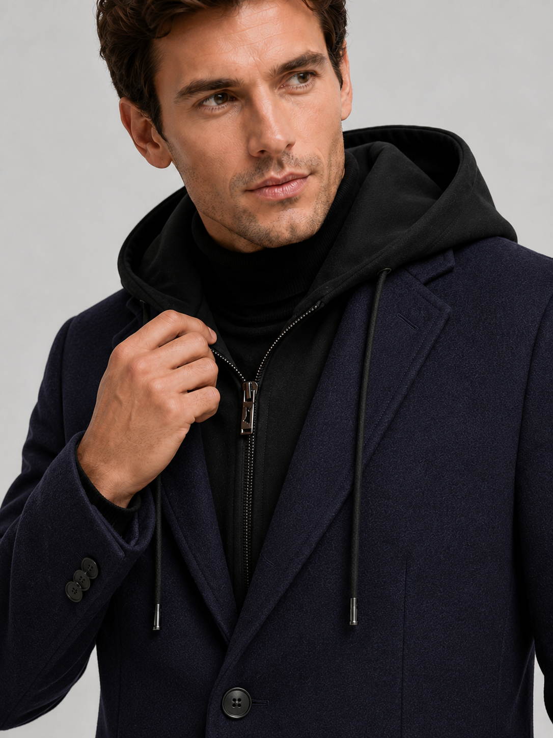 Detail photo of a man wearing a navy wool hooded trench coat, close up of the wool texture, hood, collar, buttons, cuffs, and pocket construction