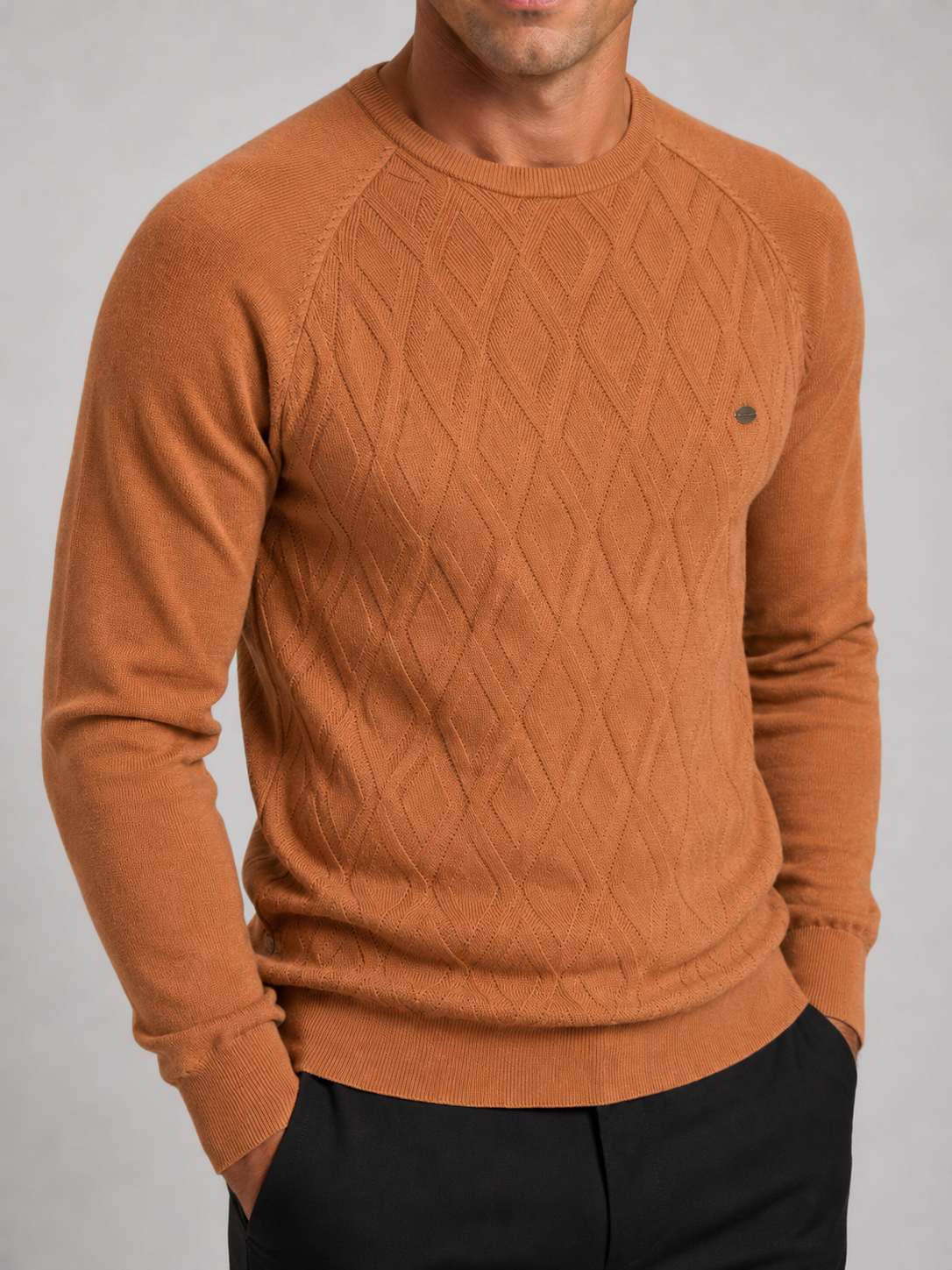 Close-up of an orange argyle sweater showing the diamond knit pattern, crew neckline, ribbed cuffs, hem, and warm texture