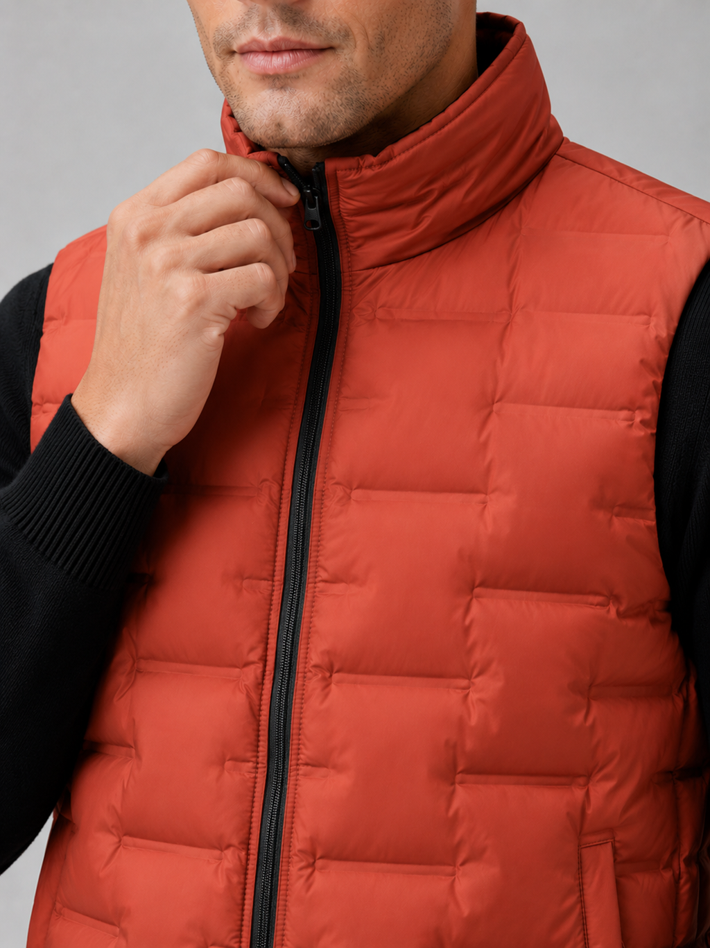 Close up of orange white duck down vest showing lightweight quilted insulation, stand collar, and weather resistant fabric detail