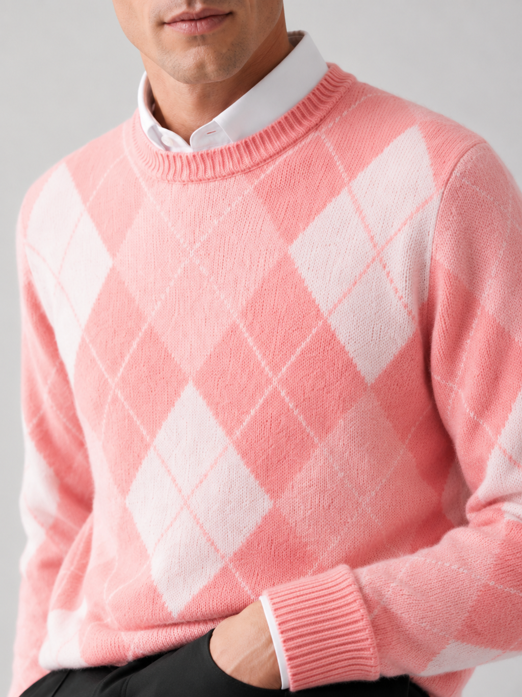 Close-up of a pink wool argyle sweater showing the diamond pattern, thick knit texture, crew neckline, ribbed cuffs, and hem