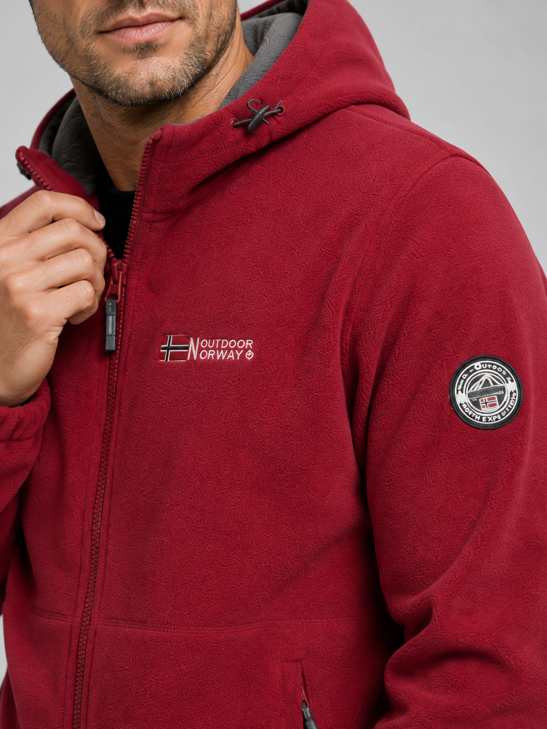 Close-up of a red hooded fleece jacket showing the soft fleece texture, windproof construction, full zipper, hood, pockets, cuffs, and stitching details