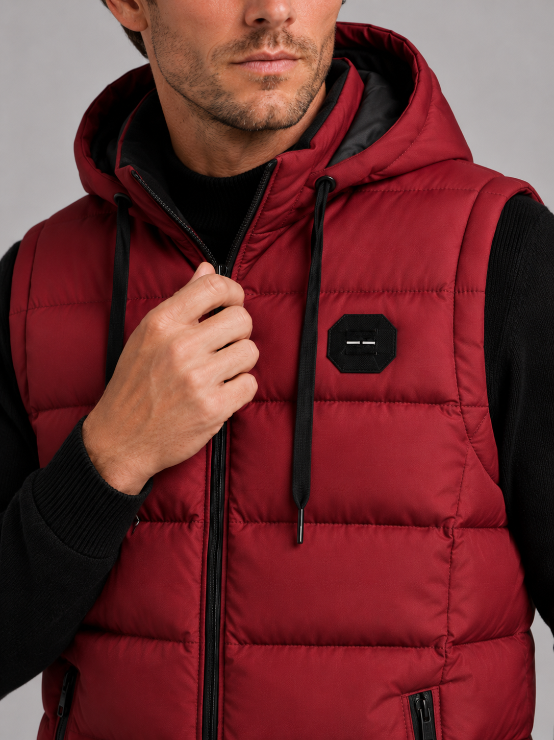 Close-up of a red hooded puffer vest showing the cotton padding, thick insulation, zipper closure, hood, pockets, armholes, and stitching details
