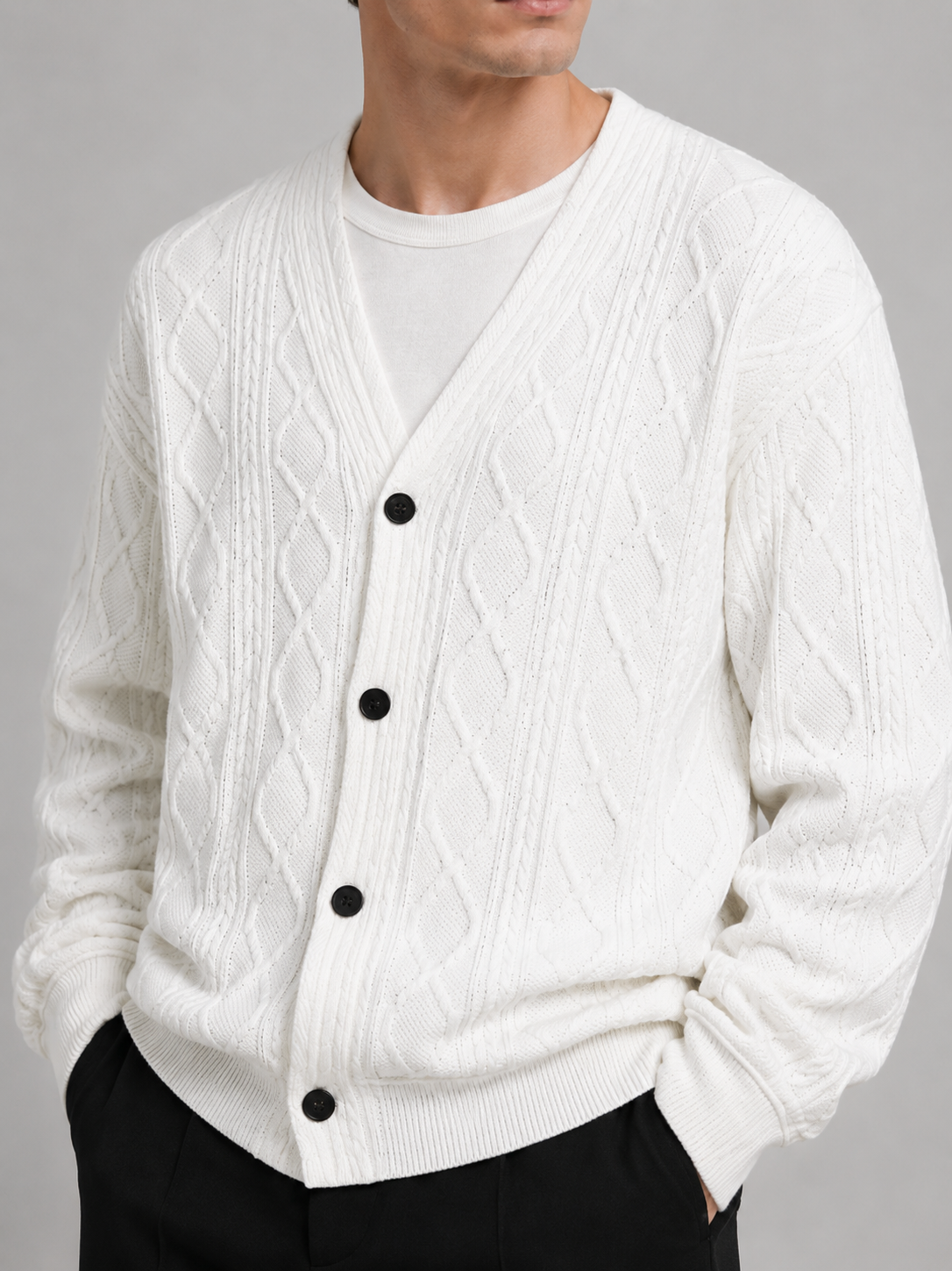 Close-up of a white cable knit cardigan showing the diamond pattern, textured cable knit, V-neckline, front buttons, ribbed cuffs, and hem