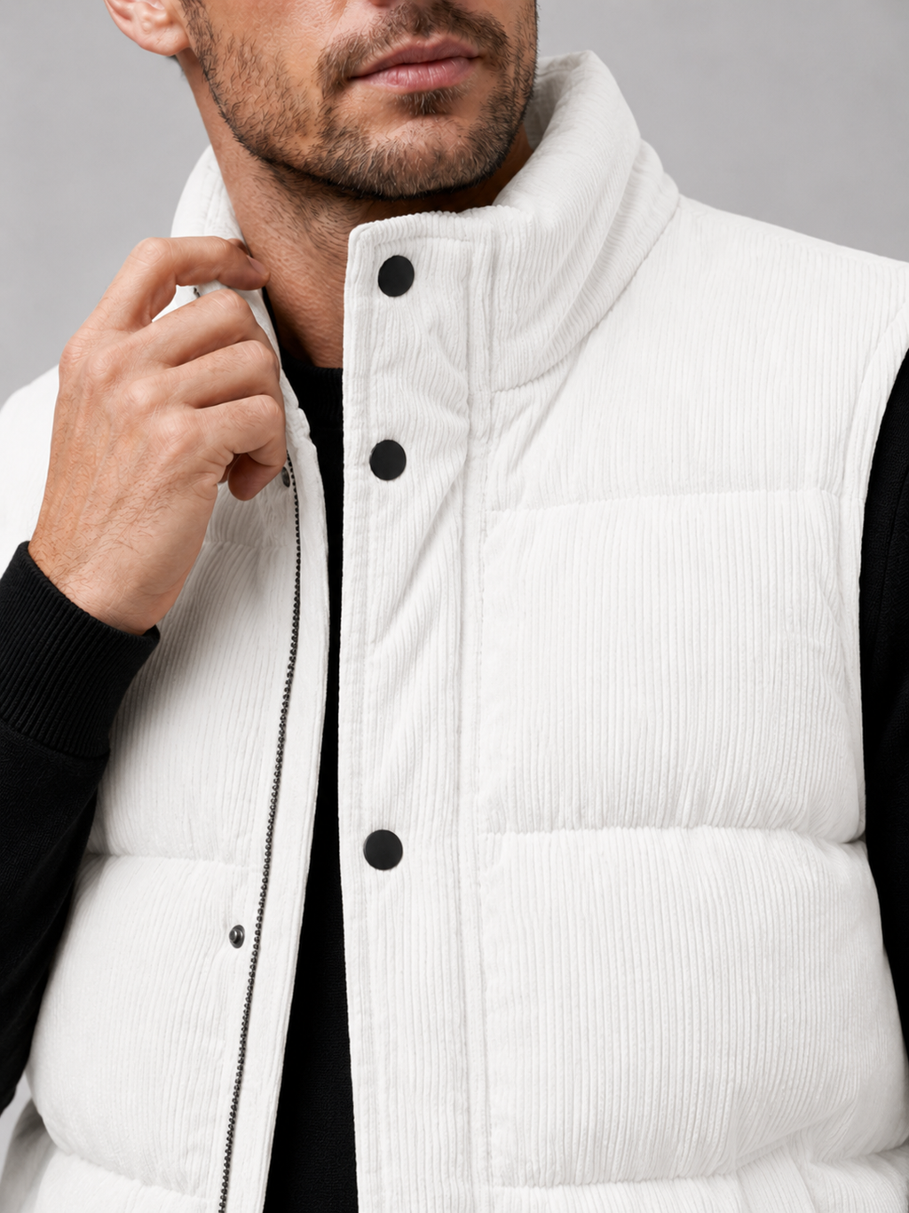 Close-up of a white corduroy puffer vest showing the ribbed fabric texture, thick padding, stand collar, zipper, pockets, armholes, and stitching