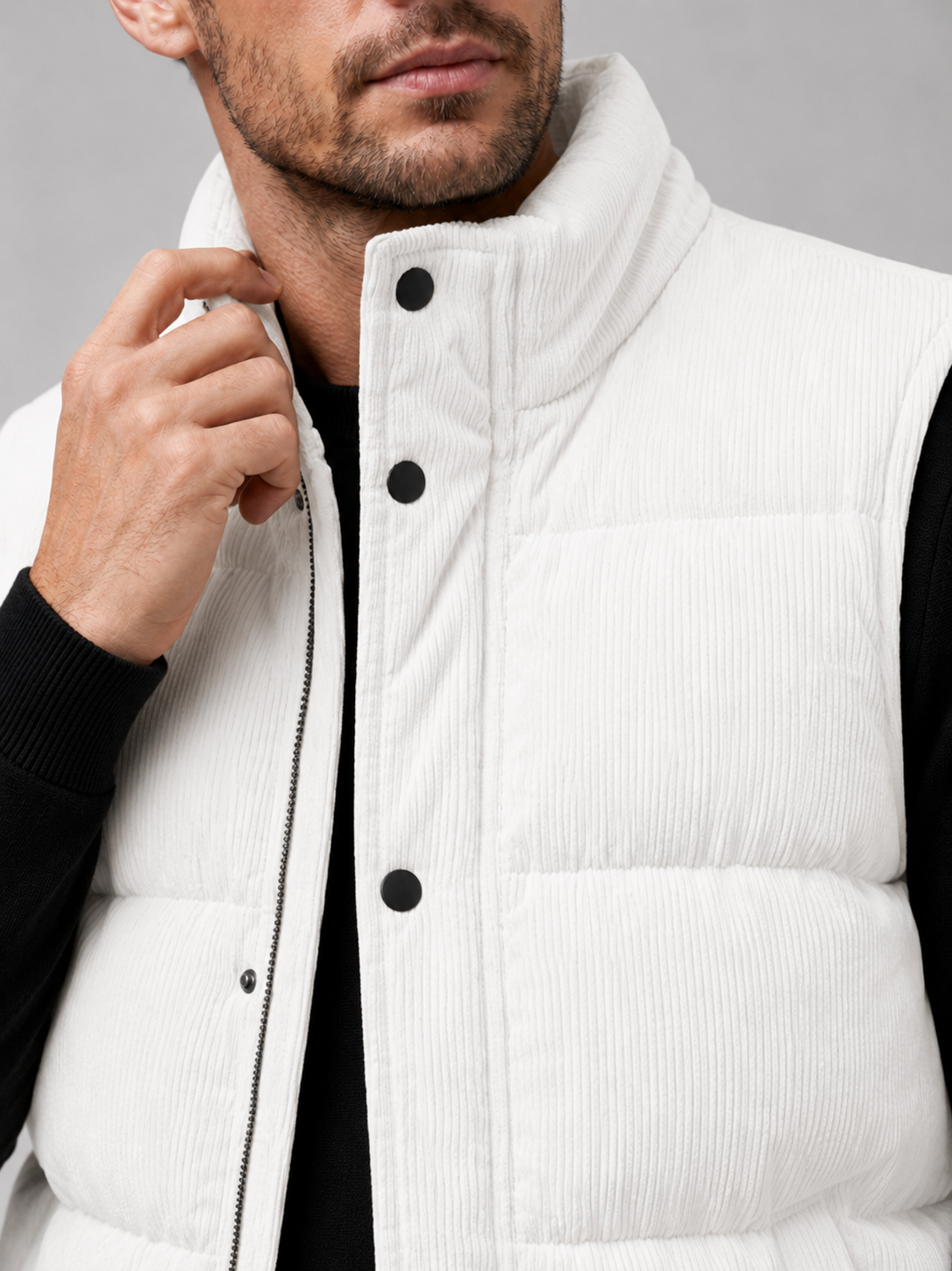 Close-up of a white corduroy puffer vest showing the ribbed fabric texture, thick padding, stand collar, zipper, pockets, armholes, and stitching