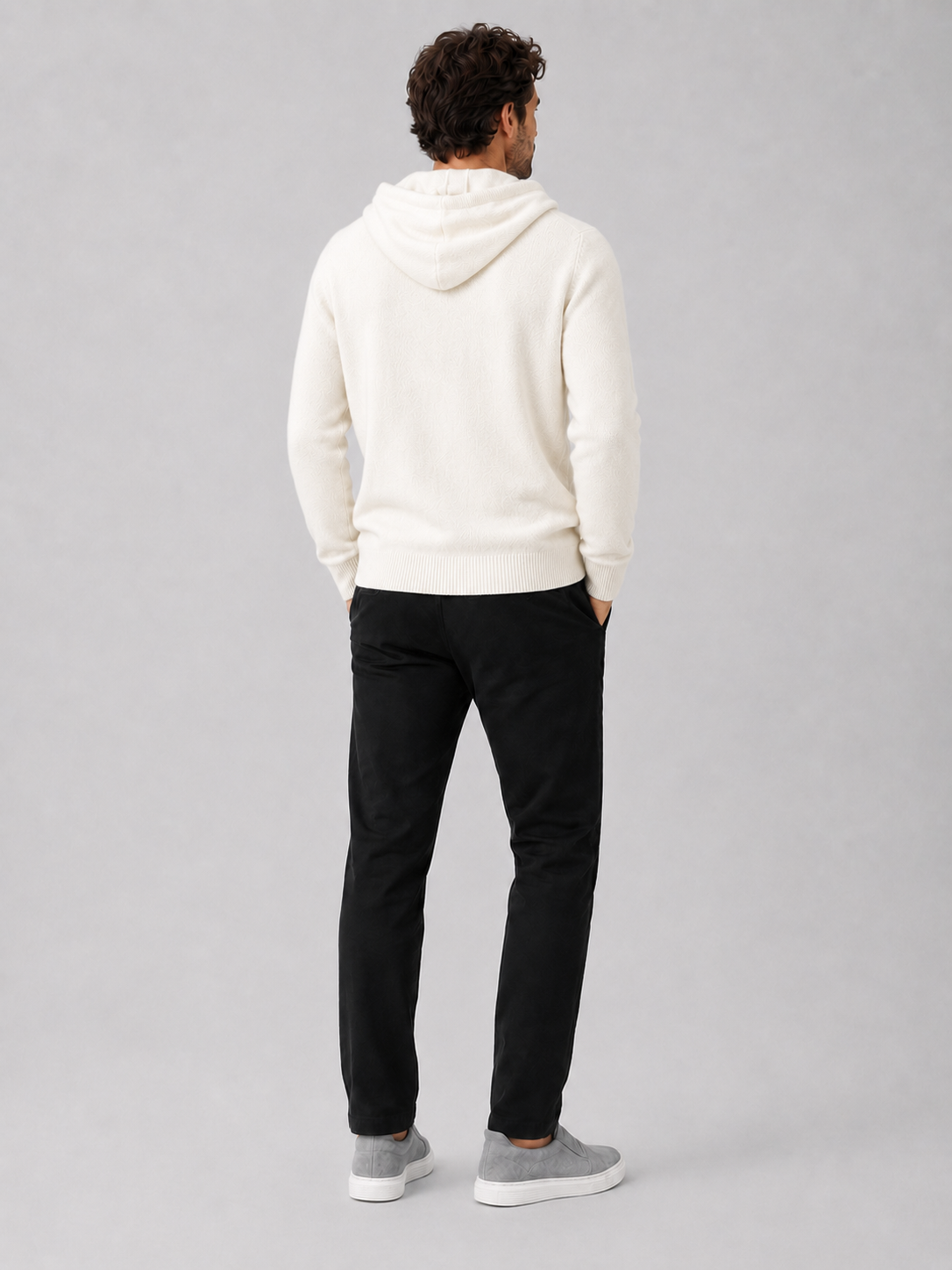 Back view of a man wearing a white wool hoodie sweater showing the attached hood, long sleeves, and relaxed fit