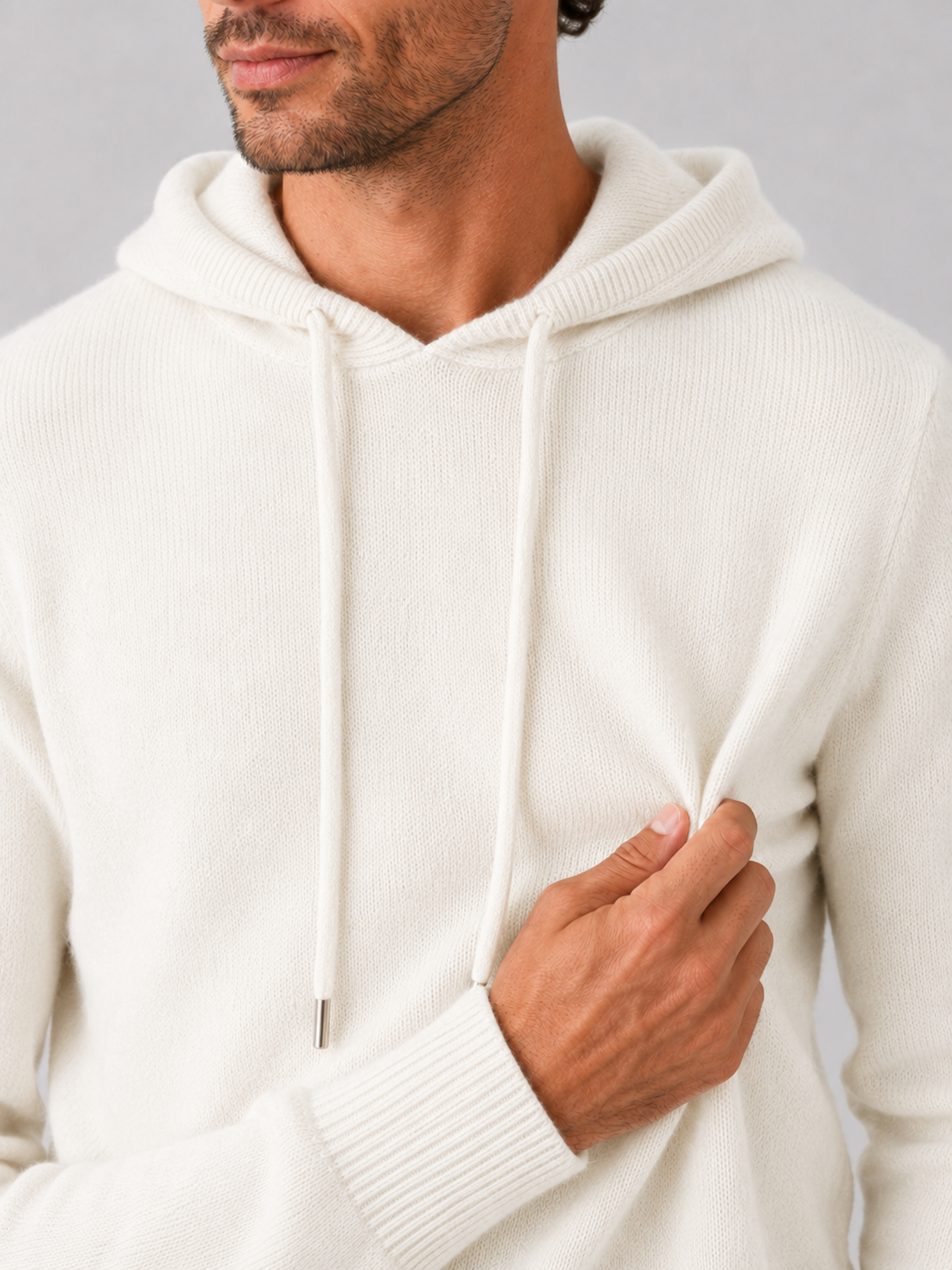 Close-up of a white wool hoodie sweater showing the soft knit texture, hood, ribbed cuffs, hem, and stitching details