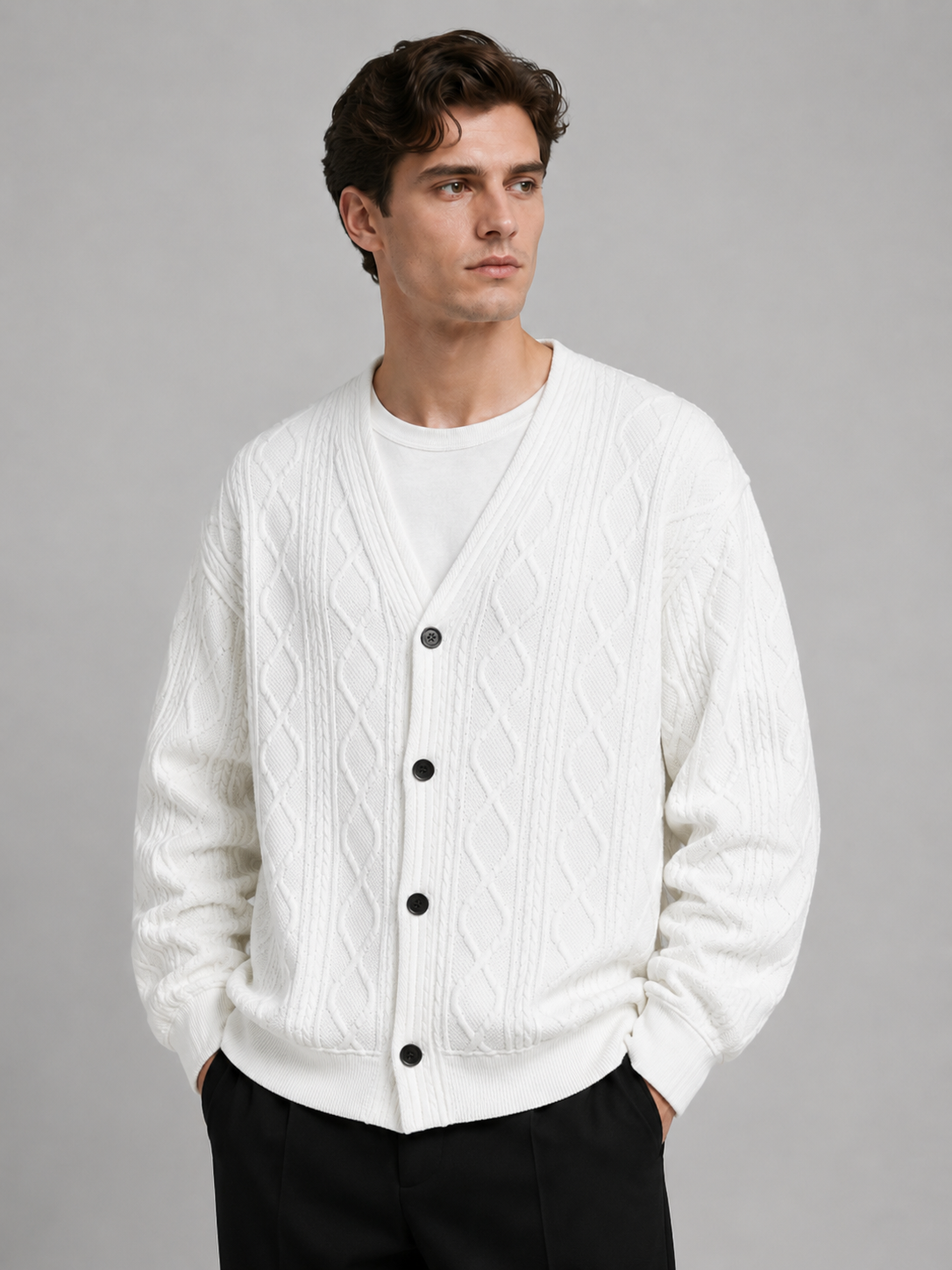 Front view of a man wearing a white cable knit cardigan sweater with a V-neck, diamond pattern, button-front design, and oversized fit