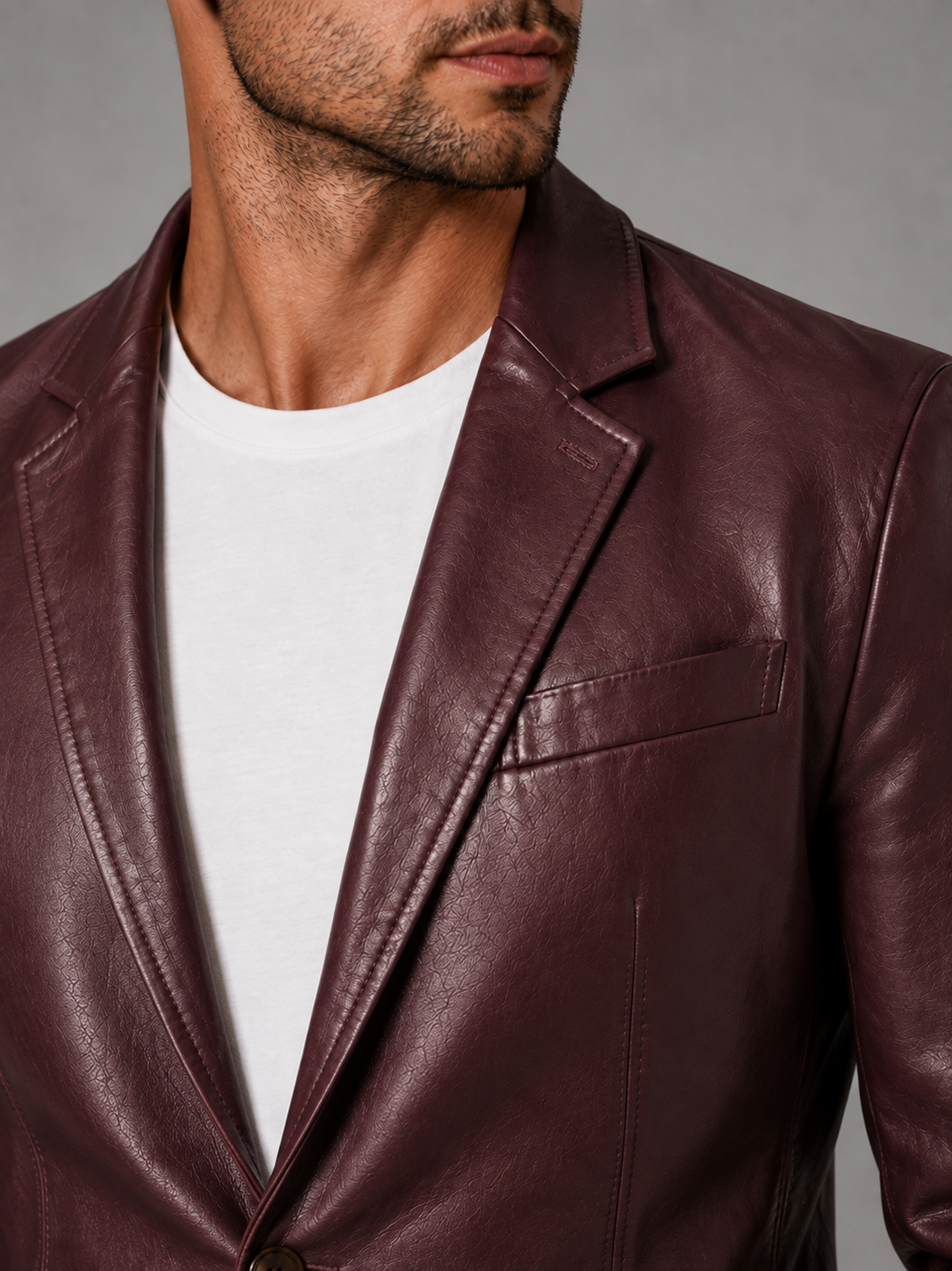 Close-up of a wine red leather blazer jacket showing the premium leather texture, notched lapel, button closure, tailored stitching, cuffs, and pocket details
